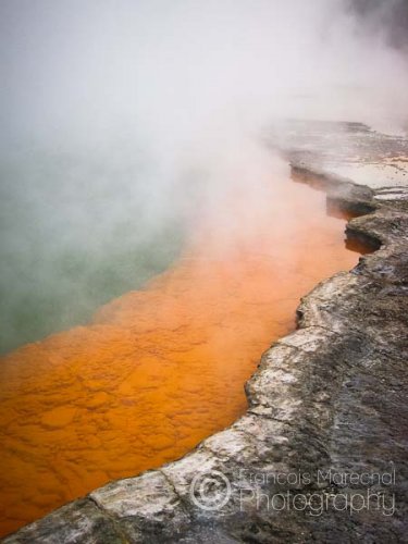 Champagne Pool is a prominent geothermal feature within the Wai-O-Tapu geothermal area. The name is derived from the abundant efflux of carbon dioxide, similar to a glass of bubbling champagne. The orange colour originates from deposits of arsenic and antimony sulfides.