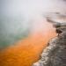 Champagne Pool is a prominent geothermal feature within the Wai-O-Tapu geothermal area. The name is derived from the abundant efflux of carbon dioxide, similar to a glass of bubbling champagne. The orange colour originates from deposits of arsenic and antimony sulfides.